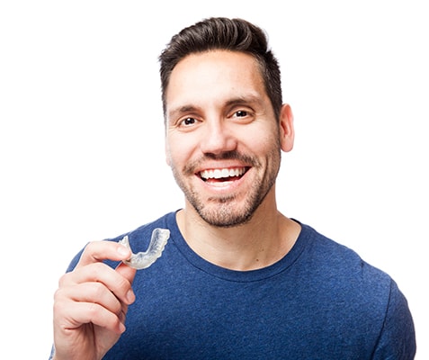 A young man with a beard and dark blue shirt holding Invisalign clear aligners